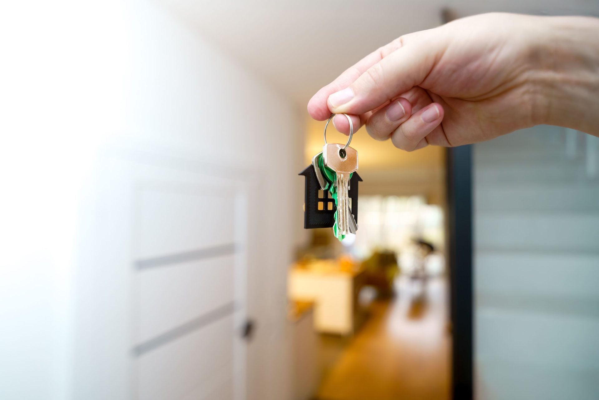 A hand holding house keys inside a modern apartment, symbolizing new property ownership or rental.